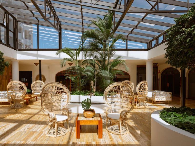 Cortile interno luminoso con tetto trasparente, mobili in rattan e piante verdi