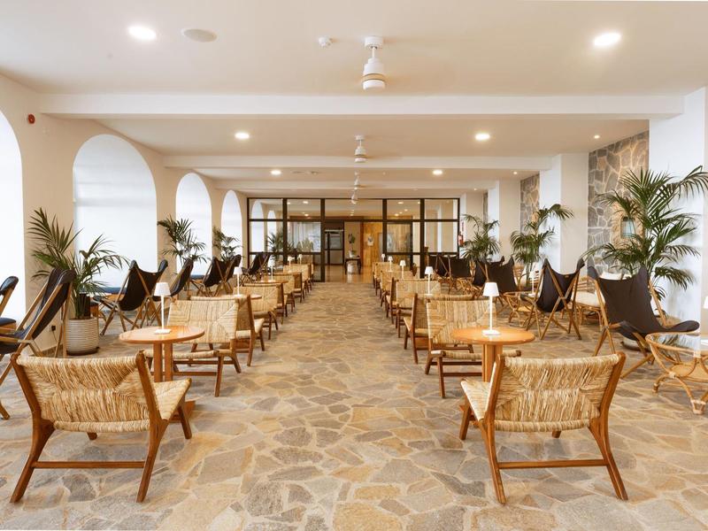 Ristorante moderno e luminoso con pavimento in pietra, sedie in legno e piante ai lati