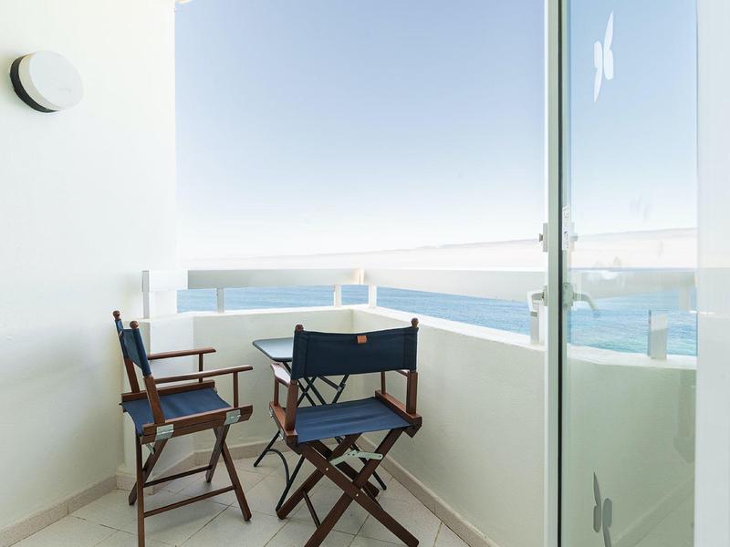 Balcone con ringhiera bianca, tre sedie pieghevoli blu e vista sul mare