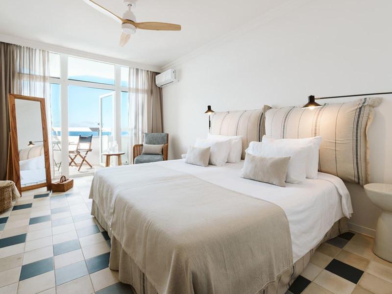 Camera d'hotel luminosa con letto matrimoniale, grande finestra e balcone con vista mare.