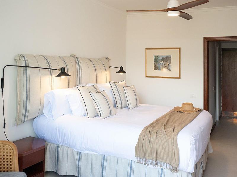 Camera d'hotel luminosa con letto matrimoniale grande, arredamento coordinato e piccolo comodino.