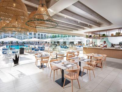 Zona pranzo all'aperto luminosa con tavoli e sedie in legno vicino a piscina e bar.