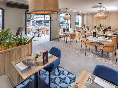 Ristorante d'hotel moderno con mobili in legno, sedie blu e moquette a motivi vicino a porte di vetro.