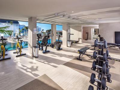 Lichte fitnessruimte met moderne apparatuur en grote ramen met uitzicht op het zwembad.