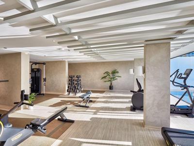 Moderne fitnessruimte met loopbanden, dumbbells en natuurlijk licht via ramen.