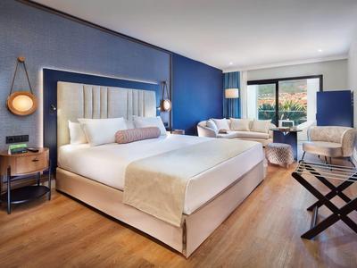 Camera d'hotel moderna con letto grande, parete blu e zona salotto vicino al balcone.