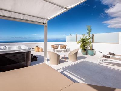 Luminoso terrazzo sul tetto con posti a sedere, vasca idromassaggio e vista sull'oceano sotto un cielo azzurro.
