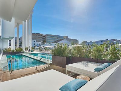 Area piscina moderna dell'hotel con lettini e edifici della città sullo sfondo.