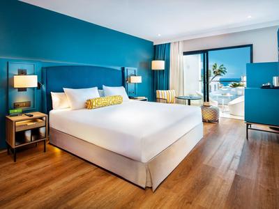 Camera d'hotel moderna con letto king, pareti blu, pavimento in legno e balcone con vista oceano.