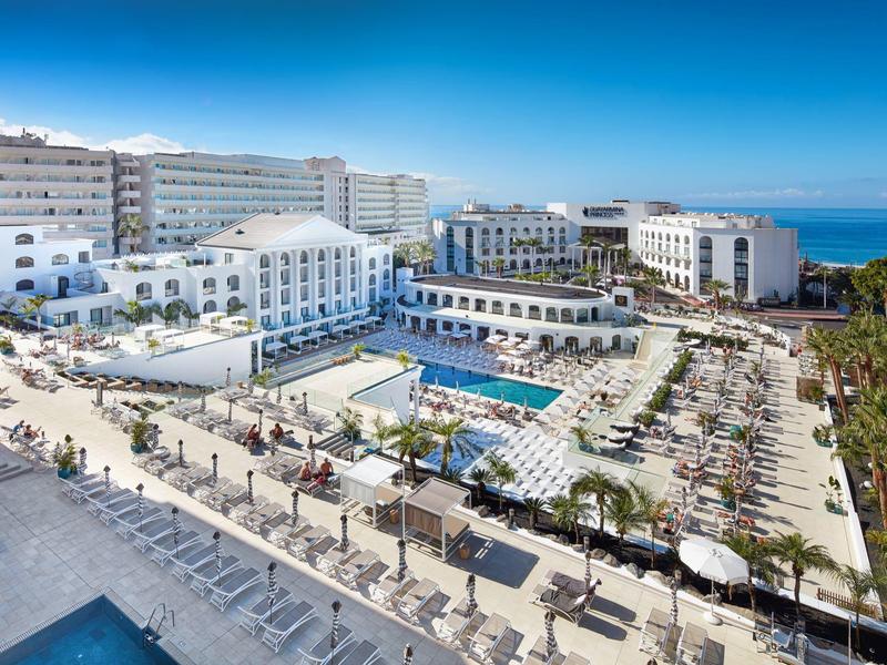 Grande hotel resort con piscine, lettini, palme e vista mare sotto un cielo limpido.
