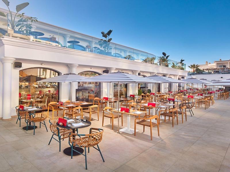 Sedie e tavoli in legno all'aperto sotto grandi ombrelloni bianchi.