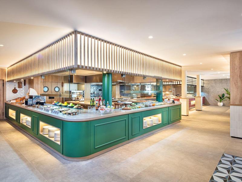 Area buffet moderna con banconi verdi e varie opzioni di cibo in una sala da pranzo spaziosa.