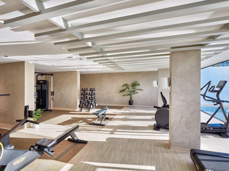 Palestra moderna con tapis roulant, biciclette da esercizio e vista sulla piscina attraverso grandi finestre.