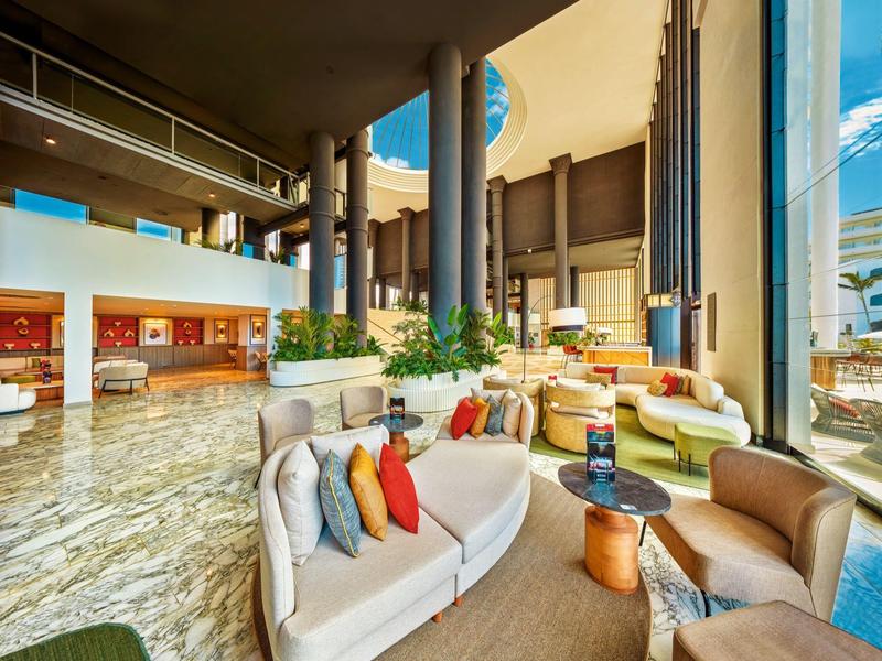 Ampia hall d'hotel con soffitti alti, cuscini colorati e aree salotto moderne.