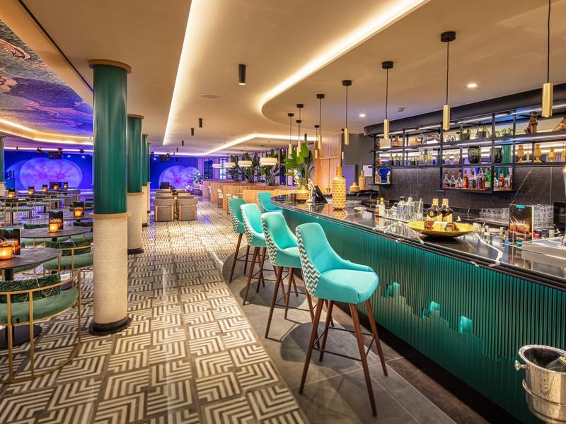 Bar moderno con sgabelli turchesi, tappeto a motivi e illuminazione elegante.