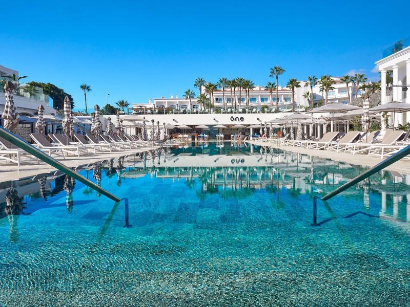 Piscina azzurra limpida con lettini e palme in un resort soleggiato.