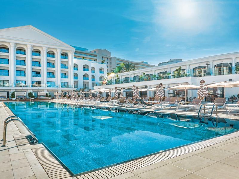 Piscina soleggiata dell'hotel con lettini e ombrelloni sotto il cielo blu.
