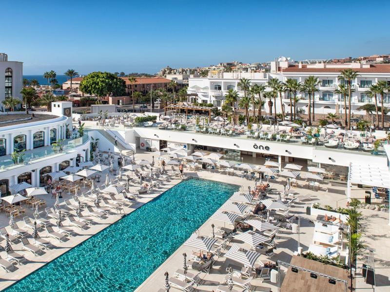 Grande piscina esterna dell'hotel con molte sdraio e palme sotto un cielo azzurro limpido