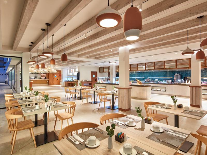 Ristorante moderno in hotel con sedie in legno, tavoli bianchi e illuminazione calda a sospensione.