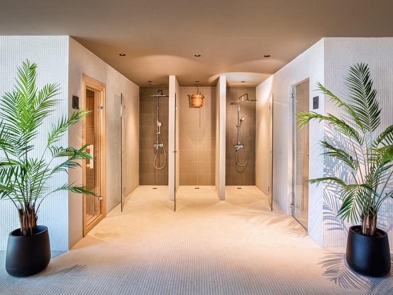 Corridoio dell'hotel con tre docce incorniciate da pareti bianche e due piante in vaso.