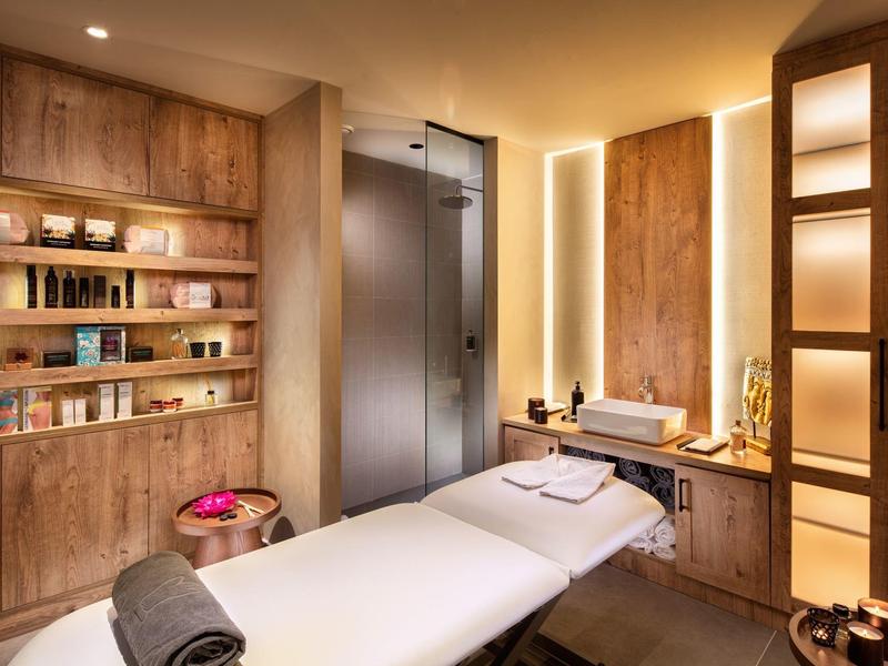 Accogliente stanza spa con lettino da massaggio, scaffali in legno e luce soffusa.