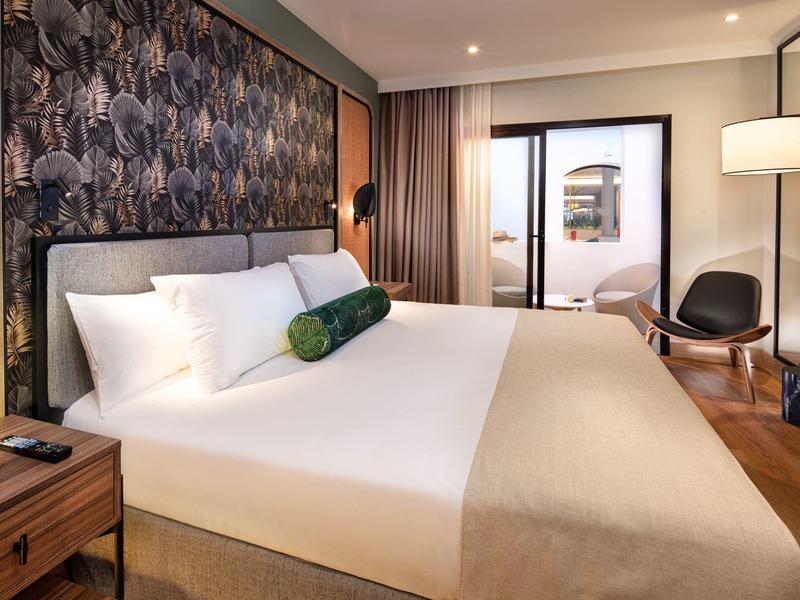 Camera d'hotel moderna con letto grande, carta da parati decorativa, finestra ampia e area salotto.