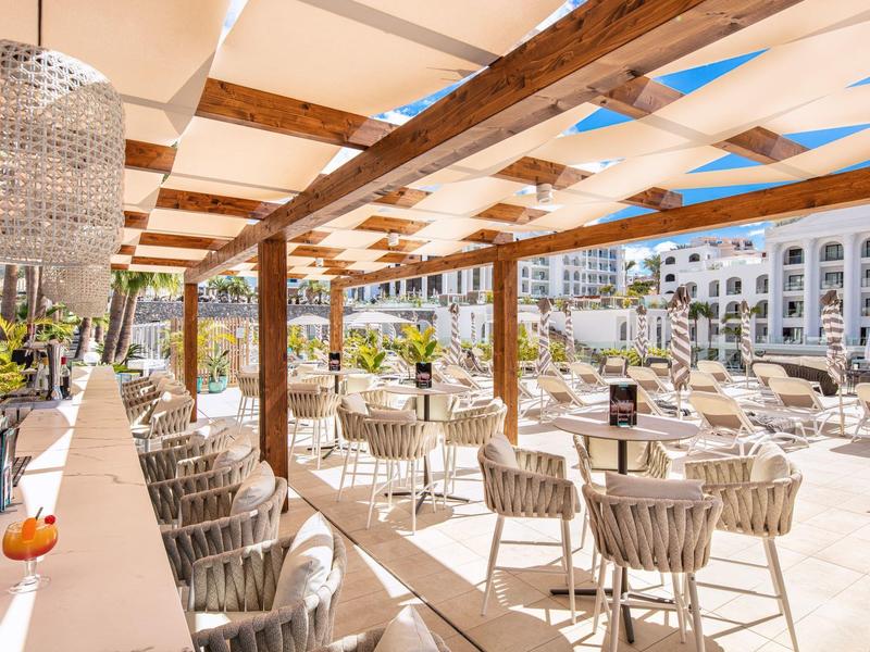 Ampia zona pranzo all'aperto con sedie in vimini e lampadari in una località soleggiata.