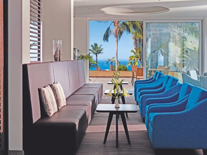 Habitación de hotel moderna con sillones azules y vista al mar a través de grandes ventanas.