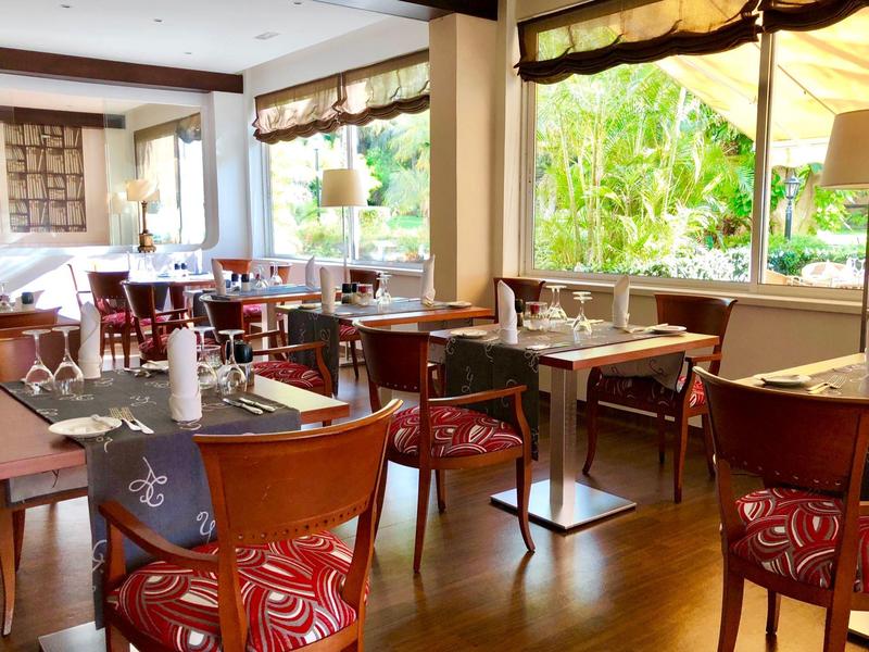 Restaurante luminoso con muebles de madera, sillas rojas y vista al verde desde las ventanas.