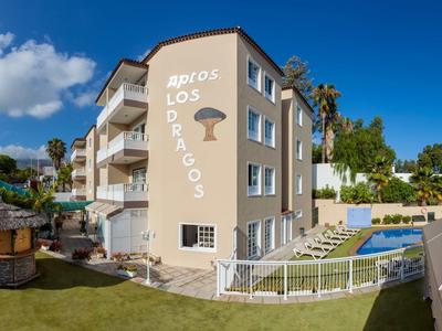 Light beige hotel with balcony views, pool area, and garden under sunny weather.