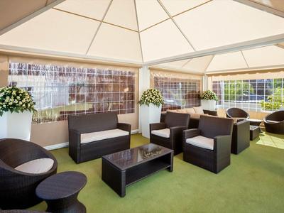 Moderní lounge s černým posezením a velkými květinovými dekoracemi pod bílým altánem.