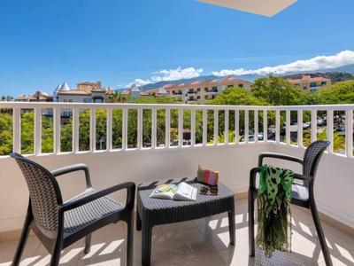 Balkon s dvěma židlemi, stolem a výhledem na zeleň a vesnici.