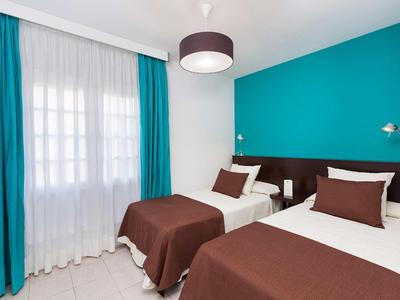 Hotelový pokoj se dvěma jednolůžky, hnědým povlečením, tyrkysovými závěsy a akcentní stěnou.