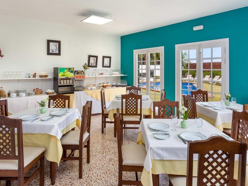 Světle zařízená snídaňová místnost s bílými a žlutými stoly a dřevěným nábytkem.