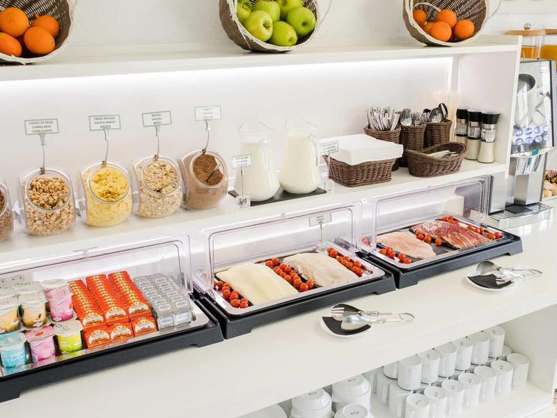 Bufet s produkty na snídani jako pečivo, uzeniny, sýry a čerstvé ovoce v miskách.