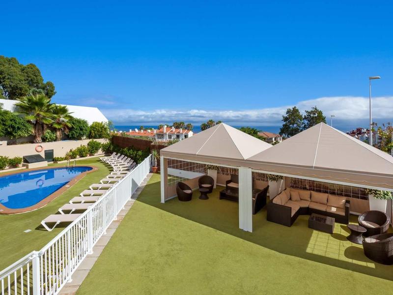 Terasa se dvěma pavilony a bazénem v udržované zahradě pod modrou oblohou.