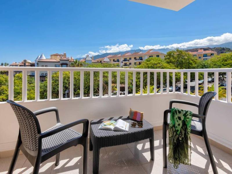 Balkon s dvěma židlemi, stolem a výhledem na zeleň a vesnici.