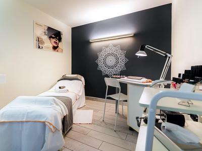 Une chambre de spa confortable avec un lit de massage, un bureau, une lampe et un mandala décoratif sur un mur sombre.