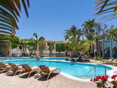 Poolbereich mit Liegestühlen und Palmen in einem sonnigen Hotelresort.