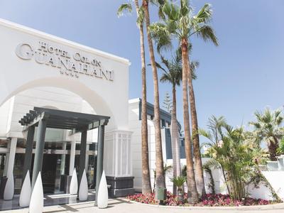 Weißes Gebäude mit Säulen, Palmen und klarem blauen Himmel im sonnigen Außenbereich.