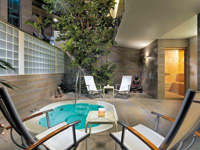 Moderner Wellnessbereich mit kleinem Whirlpool, Liegestühlen und Saunabereich unter warmem Licht.