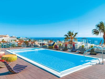 Piscine extérieure avec chaises longues et vue sur la mer sous un ciel bleu clair.