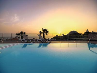 Ein ruhiger Pool bei Sonnenuntergang mit Palmen und Liegestühlen am Rand.