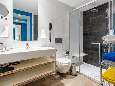 Salle de bain d'hôtel moderne avec grand lavabo, toilettes, douche en verre et serviettes colorées sur un porte-serviettes.