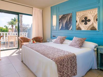 Chambre d'hôtel lumineuse avec lit double, mur bleu, balcon avec vue sur un palmier.