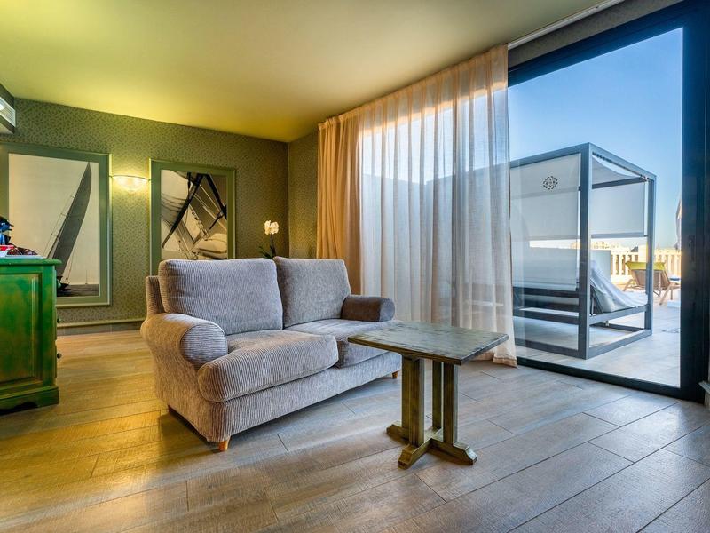 Chambre d'hôtel confortable avec canapé, table, grand miroir et balcon avec sièges extérieurs.