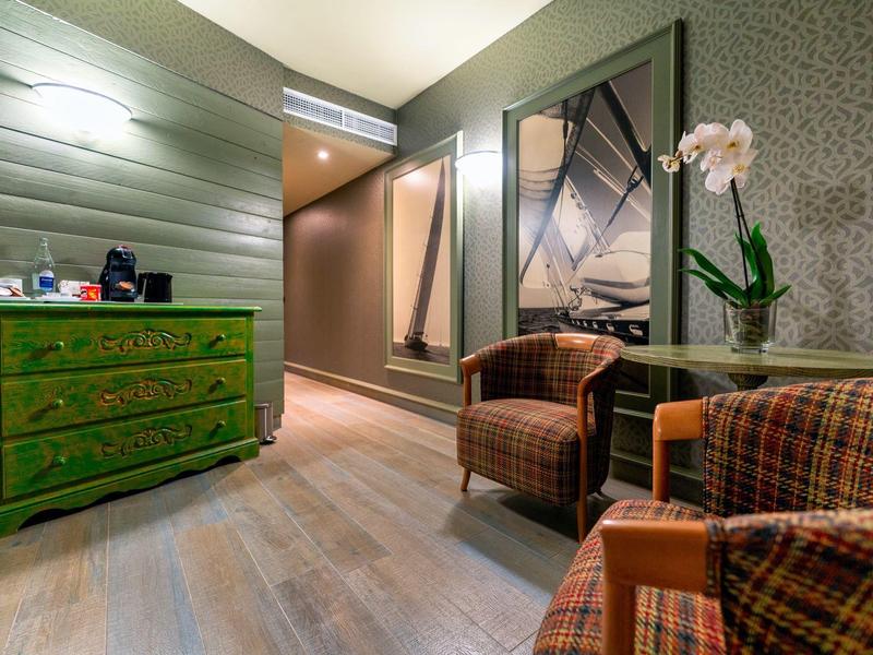 Coin salon confortable avec deux fauteuils, commode verte et orchidée dans une pièce chaleureusement éclairée.