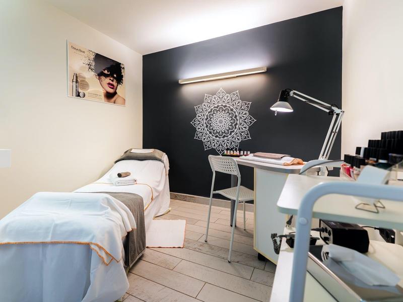 Une chambre de spa confortable avec un lit de massage, un bureau, une lampe et un mandala décoratif sur un mur sombre.