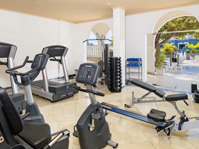 Salle de sport d'hôtel lumineuse avec vélos, tapis roulants, rameurs et poids près de la piscine.