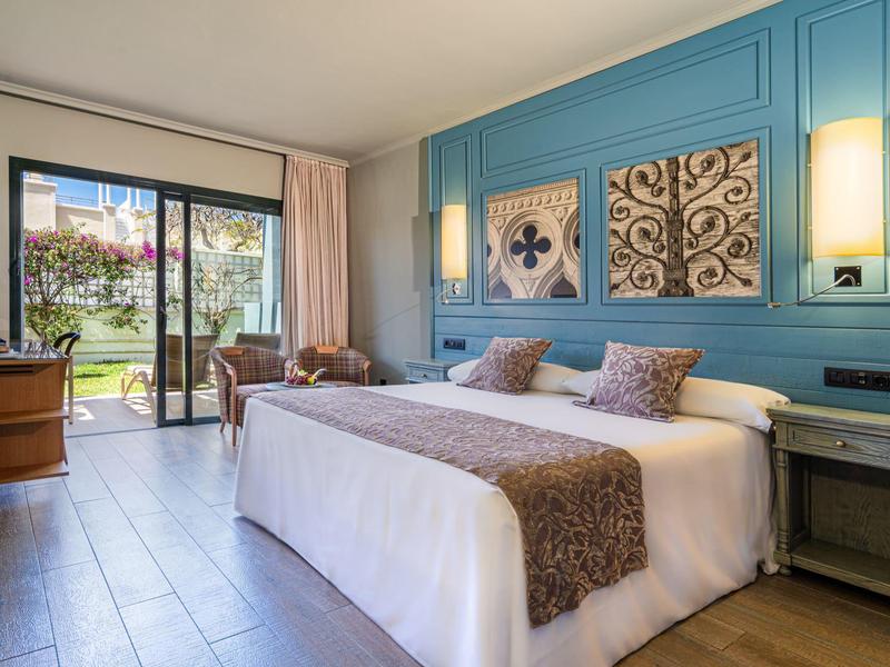 Chambre d'hôtel lumineuse avec lit king-size, mur bleu et balcon donnant sur jardin.